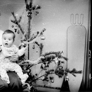 Woman holding baby near decorated Christmas tree.
