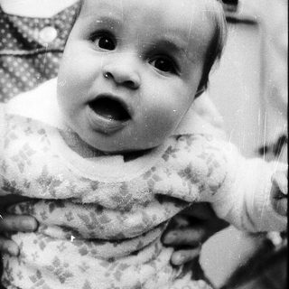 Baby with surprised expression, being held indoors.