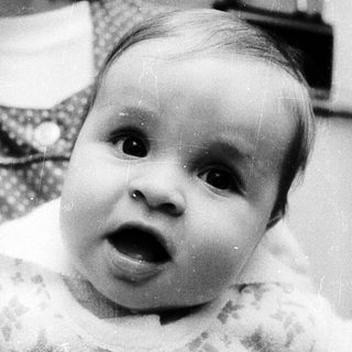 Baby with surprised expression, being held indoors.