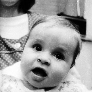 Baby with surprised expression, being held indoors.