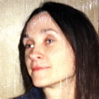 Person sitting on bed with long hair.