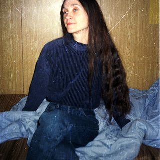 Person sitting on bed with long hair.