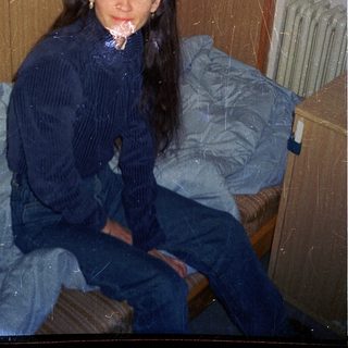 Woman sitting on bed in dimly lit room.