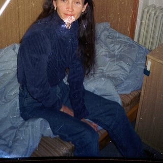Woman sitting on bed in dimly lit room.