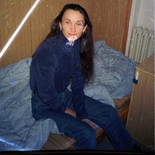 Woman sitting on bed in dimly lit room.