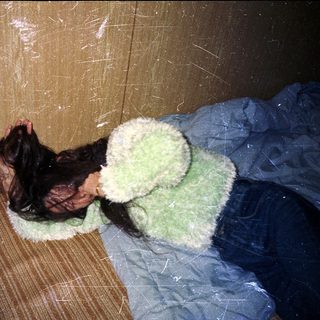 Person sleeping on wooden bench with green blanket.