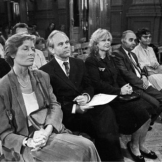 People seated in courtroom during formal proceedings.