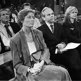 People seated in courtroom during formal proceedings.