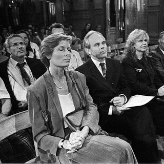 People seated in courtroom during formal proceedings.