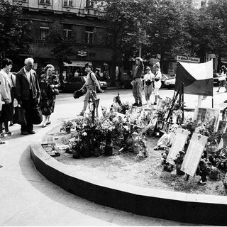 People paying respects at memorial flowers and plaques.