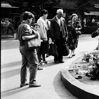 People paying respects at memorial flowers and plaques.
