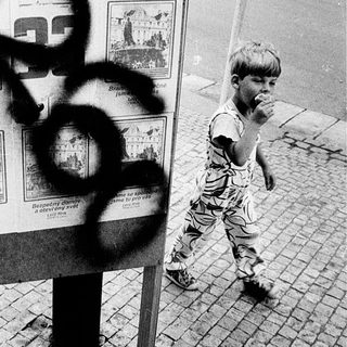 Child walking past vandalized public notice board.