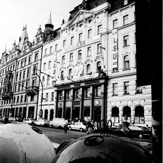 Historic European city street with grand early 20th-century buildings.