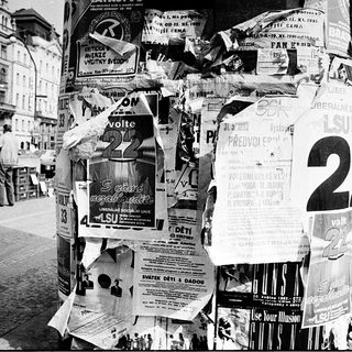 Posters covering a lamppost in urban setting.
