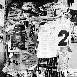 Posters covering a lamppost in urban setting.