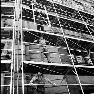 Construction workers on scaffolding performing building maintenance.
