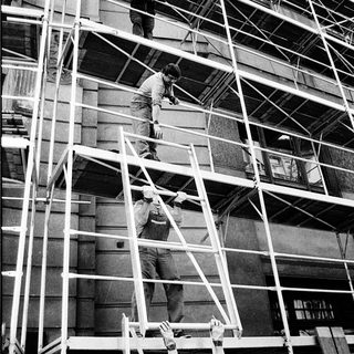 Construction workers on scaffolding performing building repairs.