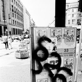 Vandalized bulletin board with graffiti in urban setting.