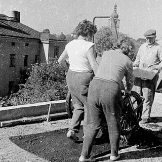 Construction workers using manual drilling equipment on pavement.