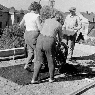Construction workers using manual drilling equipment on pavement.