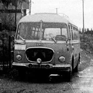 Rural village scene with old van and sheep.