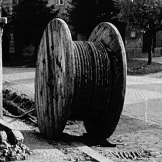 Large wooden wheel on pavement beside old buildings.