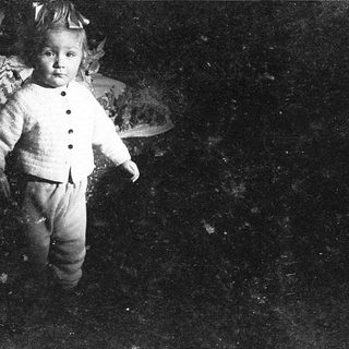 Young child dressed in vintage outfit, standing outdoors at night.