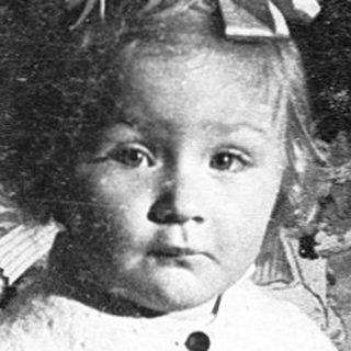 Young child dressed in vintage outfit, standing outdoors at night.