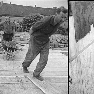 Men pushing wheelbarrows near wooden barracks.