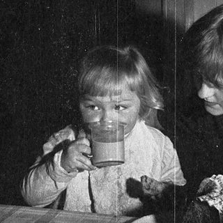 Two children drinking from cups indoors.
