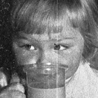 Two children drinking from cups indoors.