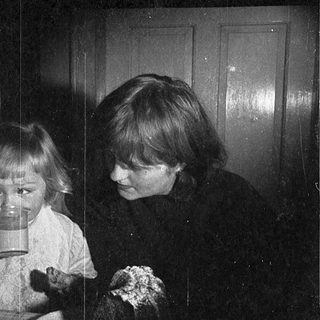 Two children drinking from cups indoors.