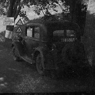 Vintage car on winding road near construction sign.