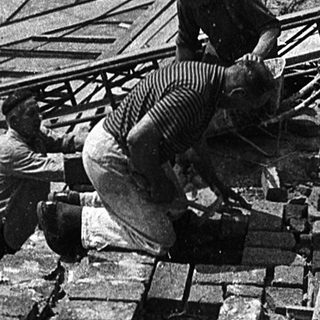 Construction workers assembling wooden beams. Historic stone archway in rural village.