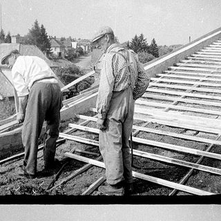 Two men installing wooden shingles on a roof.