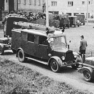Military trucks and vehicles in rural area during mid-20th century.