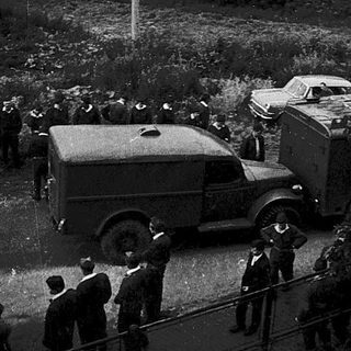 Historical outdoor gathering with crowd and vintage vehicles.