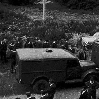 Historical outdoor gathering with crowd and vintage vehicles.