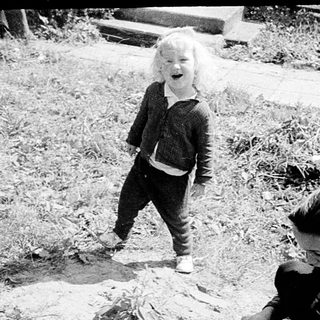 Child playing outdoors while adult kneels nearby.
