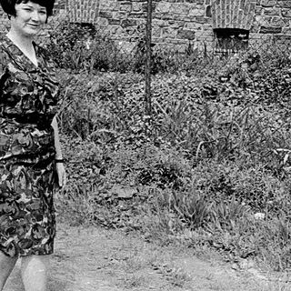 Upside-down car in grassy area, woman standing nearby.
