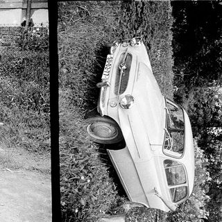 Upside-down car in grassy area, woman standing nearby.