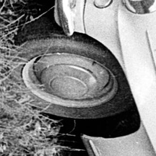 Upside-down car in grassy area, woman standing nearby.