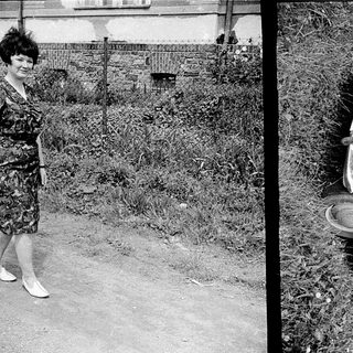Upside-down car in grassy area, woman standing nearby.