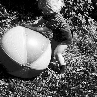 Two children playing with large beach balls outdoors.