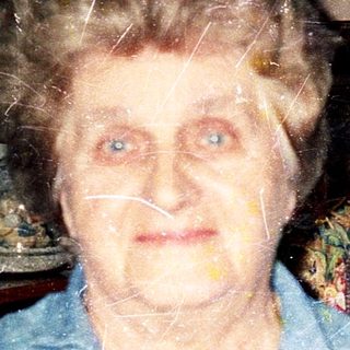 Elderly woman indoors, wearing blue shirt.