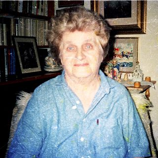 Elderly woman indoors, wearing blue shirt.