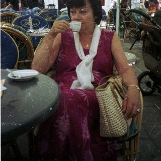 Woman sipping coffee outdoors under umbrellas.