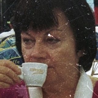 Woman sipping coffee outdoors under umbrellas.