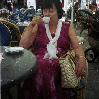 Woman sipping coffee outdoors under umbrellas.