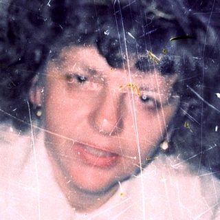 A person wearing a white sweater through frosted or cracked glass.